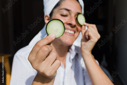 Latin adult woman applying facial mask on face with cucumber slices for exfoliation at home in Mexico Latin America, hispanic people