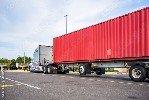 Gray big rig high cab semi truck with truck driver sleeping compartment transporting loaded container standing for rest on the industrial parking lot