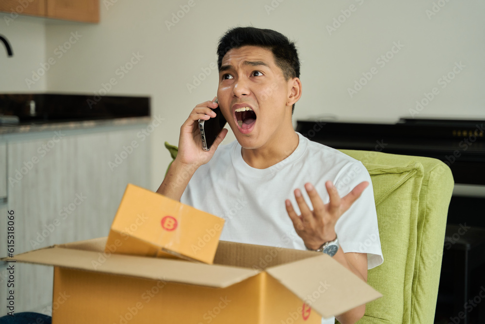 Young asian man unpacking awaited parce looking inside, sitting at sofa, unsatisfied customer opening cardboard box with online store order ,Delivery service concept. Young asian man unpacking awaited parce looking inside, sitting at sofa, unsatisfied customer opening cardboard box with online store order ,Delivery service concept.