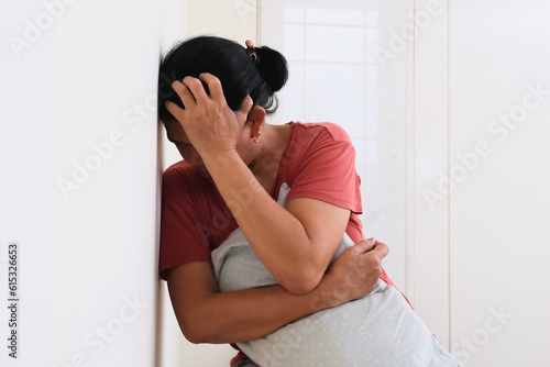 A middle-aged woman hugging a pillow while one hand on her head photo