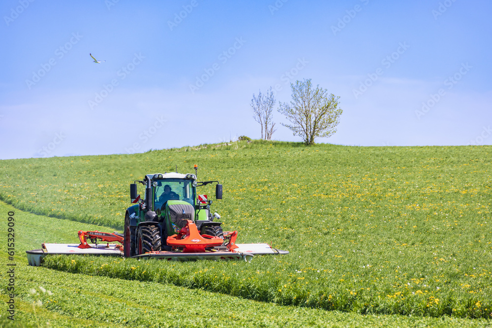 Obraz premium Tractor with a grass mower on a field on a summer day