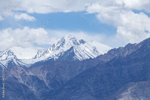 A hazy shot of snow-capped Himalaya peaks with cloudy blue sky.