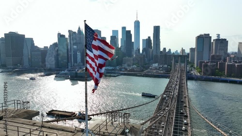 American flag waving on bright, sunny day in New York City. Brooklyn Bridge with lower Manhattan, financial district skyline in background. Aerial establishing shot in slow motion.