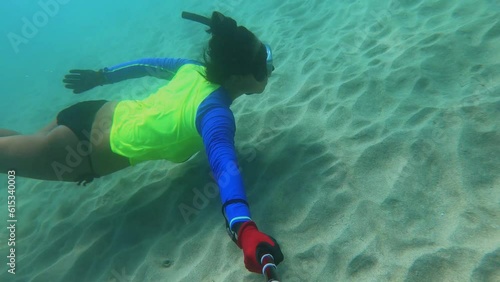 selfie of side view of an asian female free diver wearing bikini wet suit and snorkel mask in the ocean water diving swimming kicking fins holding breath at the sandy sea bed with no creatures fishes photo