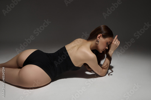 Sexy woman lying on the floor in a black bodysuit, studio portrait. Perfect body the figure of a young woman