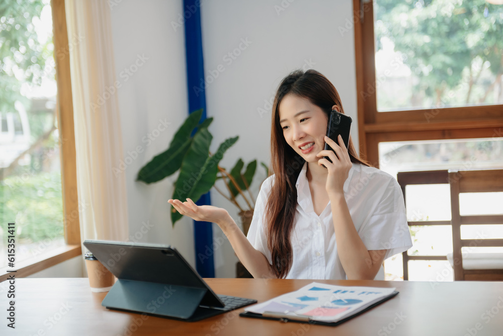 Business asian woman Talking on the phone and using a laptop with a smile while sitting at office.. Business asian woman Talking on the phone and using a laptop with a smile while sitting at office..