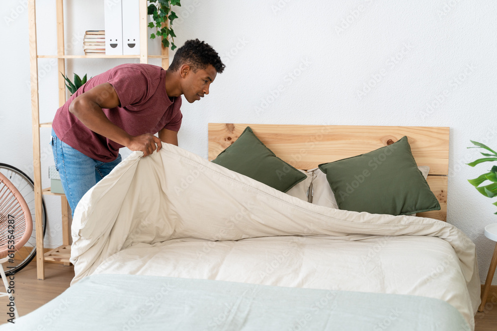 Young man making the bed in his room. Young man making the bed in his room.