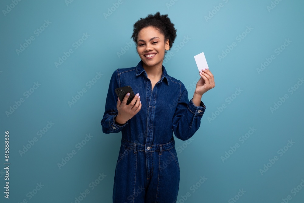 young charming brunette latin woman in blue denim suit holding credit card mockup and smartphone young charming brunette latin woman in blue denim suit holding credit card mockup and smartphone