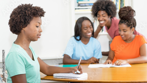 Working black female student at desk with group of learning african american students