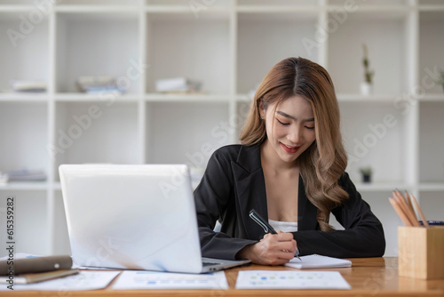 young asian woman sitting and taking note at house. Happy smiling working online, Freelance work at home © chartchai
