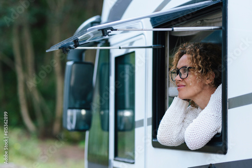 Happy camper van tourist enjoying nature outside having relax at the vehicle window. Concept of alternative vacation with motorhome and vanlife lifestyle. One woman smile and have serene expression