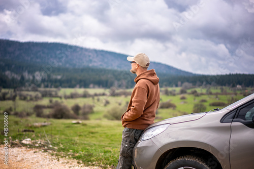 Adult caucasian middle aged male traveler standing next to the car and admiring the mountain