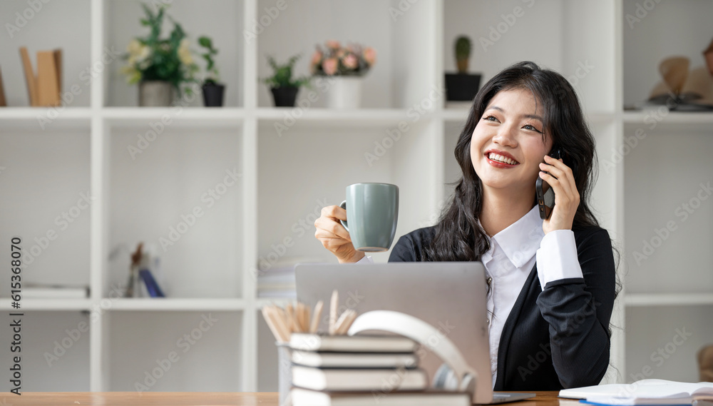Smiling young businesswoman holding mug and using smart phone sitting at home office Smiling young businesswoman holding mug and using smart phone sitting at home office