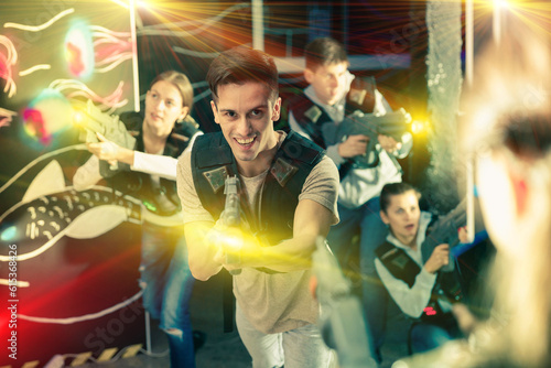 Portrait of happy young man with laser pistol and playing laser tag with his friends in dark room. High quality photo