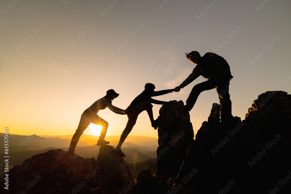 Fototapeta premium Silhouette of Hikers climbing up mountain cliff. Climbing group helping each other while climbing up in sunset. Concept of help and teamwork.
