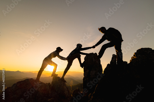 Silhouette of Hikers climbing up mountain cliff. Climbing group helping each other while climbing up in sunset. Concept of help and teamwork.