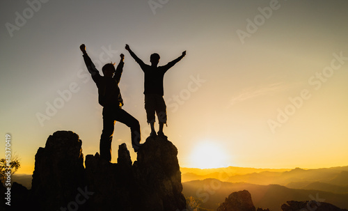 Silhouette of Hikers climbing up mountain cliff. Teamwork of two men hiker helping each other on top of mountain climbing team beautiful sunrise landscape.