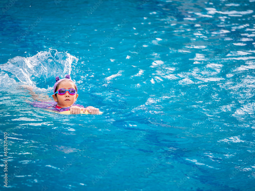 Fototapeta premium Asian child or kid girl wearing swimming suit to learning on swimming pool , learn and training swim on kick board