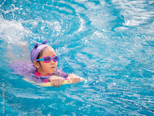 Asian child or kid girl wearing swimming suit to learning on swimming pool , learn and training swim on kick board