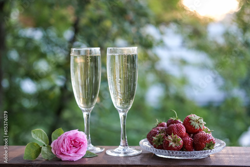 Glasses of champagne and strawberries on a terrace in a summer garden against the backdrop of evening sunlight