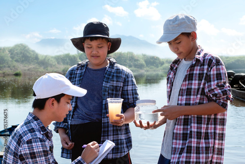 Asian boys hold magnifying glass, notebook, pen and transparent plastic tube which has clear water and cloudy water inside to compare and to do the water experiment in the river, nature study concept. © Sophon_Nawit