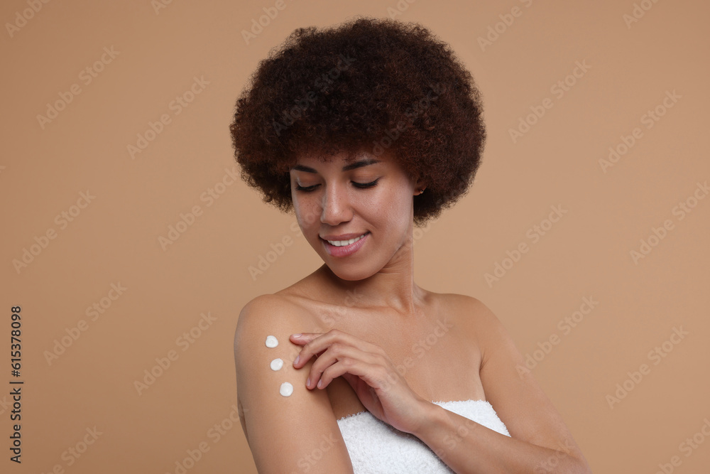 Beautiful young woman applying body cream onto arm on beige background Beautiful young woman applying body cream onto arm on beige background