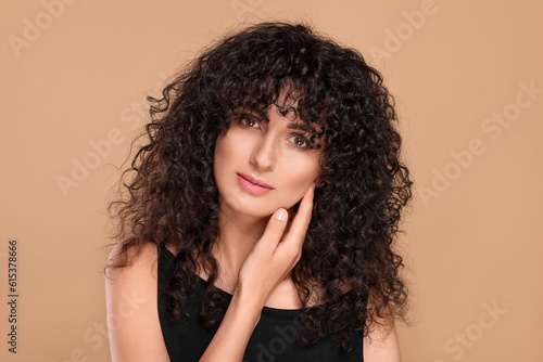 Beautiful young woman with long curly hair on beige background