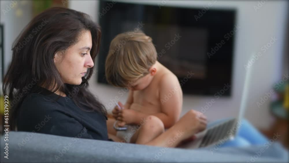Mother multi tasking with baby toddler at home using computer laptop. Candid authentic and real life mom working and parenting Mother multi tasking with baby toddler at home using computer laptop. Candid authentic and real life mom working and parenting