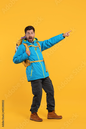 Emotional man with backpack pointing at something on orange background. Active tourism