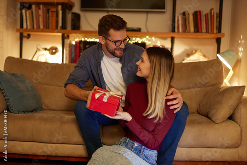 Fotografi Cheerful young woman receiving a gift from her boyfriend at home