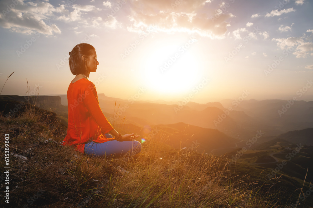 woman practices yoga and meditates on a mountain. Side view of a yogi practicing in the mountains at dawn in the rays of the sun receiving the energy of a new day