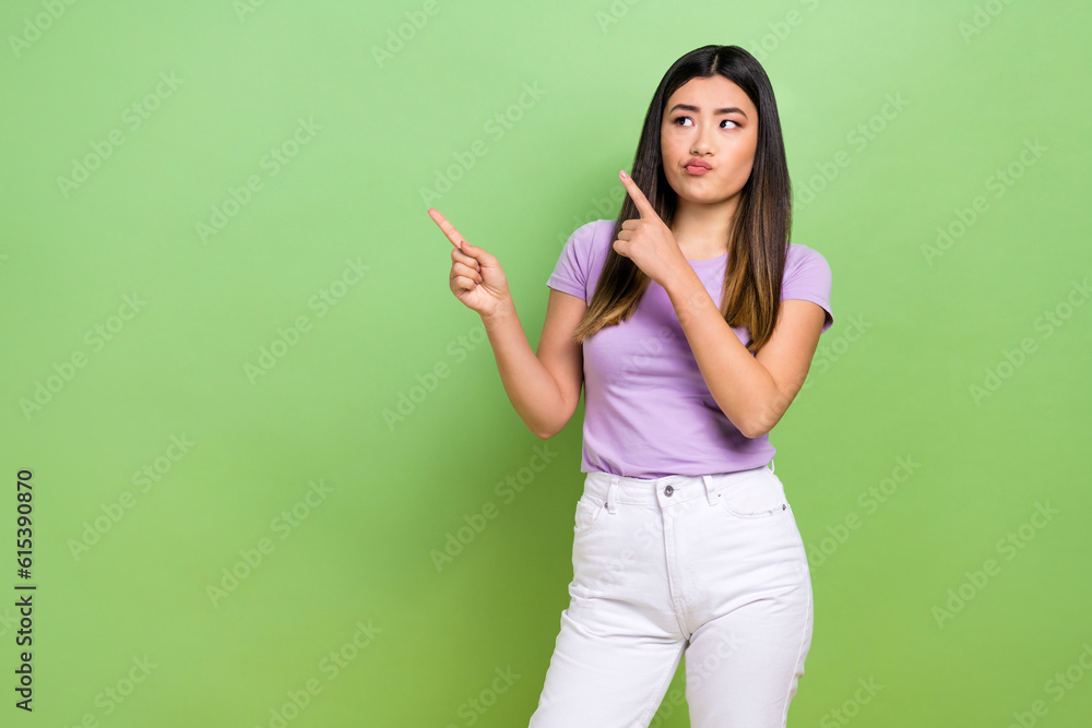 Photo of pretty vietnamese chinese young girl skeptical point empty space dressed stylish violet outfit isolated on green color background Photo of pretty vietnamese chinese young girl skeptical point empty space dressed stylish violet outfit isolated on green color background