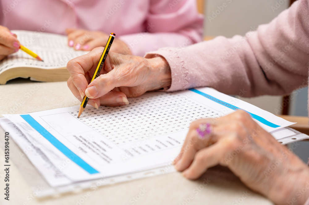 Hands of senior people solving together a word search quiz at nursing home. High quality photo Hands of senior people solving together a word search quiz at nursing home. High quality photo