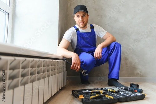 young man plumber checking radiator while installing heating system in apartment