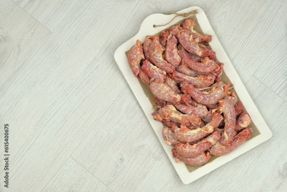 Chicken necks on a ceramic board on wood background. Chicken raw meats. Top view.