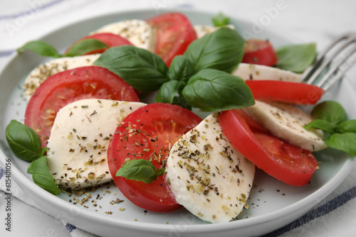 Caprese salad with tomatoes, mozzarella, basil and spices on table, closeup