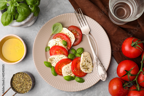 Delicious Caprese salad with tomatoes, mozzarella, basil and spices served on light grey table, flat lay