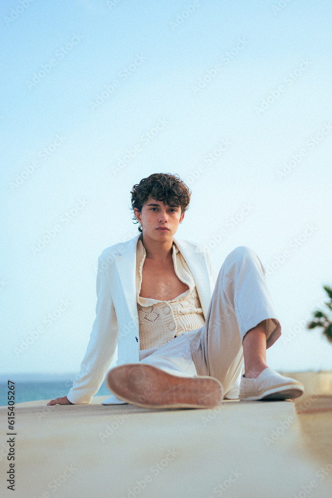 Young fashionable man poses in white clothes with the sea on the background