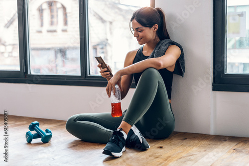 Sporty young woman using her mobile phone while holding protein shake after gym exercicis at home