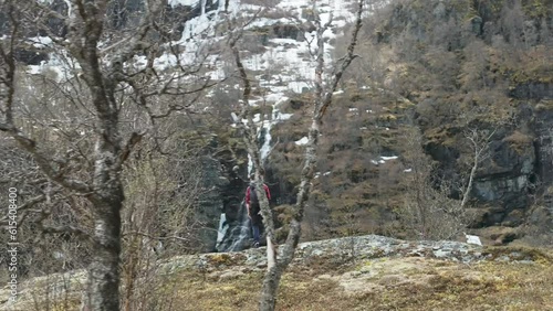 Hiker with Norwegian flag on mountain by scenic waterfall; drone telezoom reveal photo
