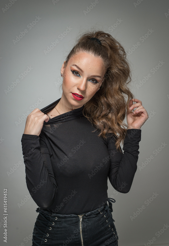 Attractive woman in black blouse and red lips posing challenging in front of a background. Classic boudoir scene. Sensual young woman with long curly hair and black jeans wearing in front of camera Attractive woman in black blouse and red lips posing challenging in front of a background. Classic boudoir scene. Sensual young woman with long curly hair and black jeans wearing in front of camera