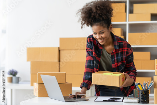 African american young woman startup business concept ecommerce business owner online on laptop Work on packing products, parcel boxes, recording customer address information for packaging delivery.