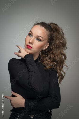 Attractive woman in black blouse and red lips posing challenging in front of a background. Classic boudoir scene. Sensual young woman with long curly hair and black jeans wearing in front of camera