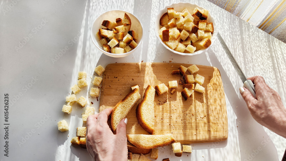 Homemade cooking and cutting of slices of diced dry white rye bread on cutting board and white plate. Hand of woman with Crackers for food, healthy eating on table in sunny day, top view Homemade cooking and cutting of slices of diced dry white rye bread on cutting board and white plate. Hand of woman with Crackers for food, healthy eating on table in sunny day, top view