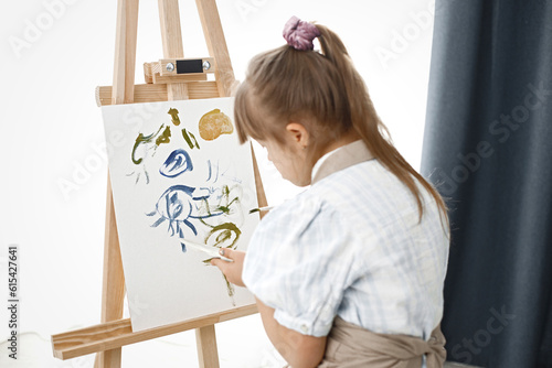 Girl with Down syndrome wearing beige apron painting on an easel