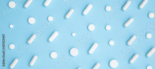 Various white medication tablets and capsules on blue background. Concept of healthcare and medicine. Top view, pattern