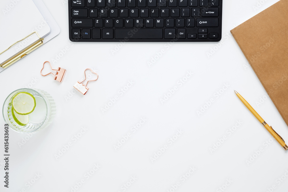 Workplace with white notebook, black keyboard, stationery, glass of water with lime and glasses on white desk. Flat lay office desk, mock up space for text. Top view. Copy space