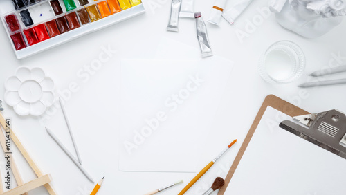 Watercolor, clipboard and other artistic accessories on a white background. Artist's desk workplace. Top view, copy space, flatlay