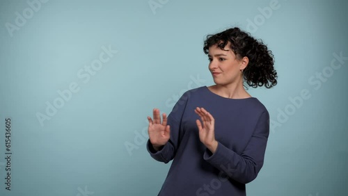 Portrait curly woman need distance showing no stop hands gesture looking at camera. Female wearing blue sweater express no way, no thanks or I don't need it sign on isolated light blue background