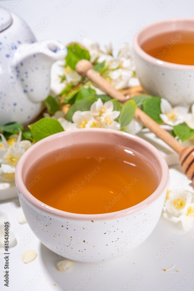 Organic herbal health drink. Jasmine flowers green tea, in white mugs, with teapot, on white table, with blooming jasmine flowers Organic herbal health drink. Jasmine flowers green tea, in white mugs, with teapot, on white table, with blooming jasmine flowers